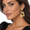 Gold plated brass teardrop earrings with textured circular discs and teardrop stud tops, resting on white fabric beside an open book.